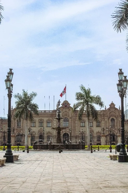 Palacio de Gobierno del Perú en la Plaza de Armas de Lima Fachada principal del Palacio de Gobierno con la bandera de Perú, la pileta de bronce y palmeras en la Plaza Mayor de Lima